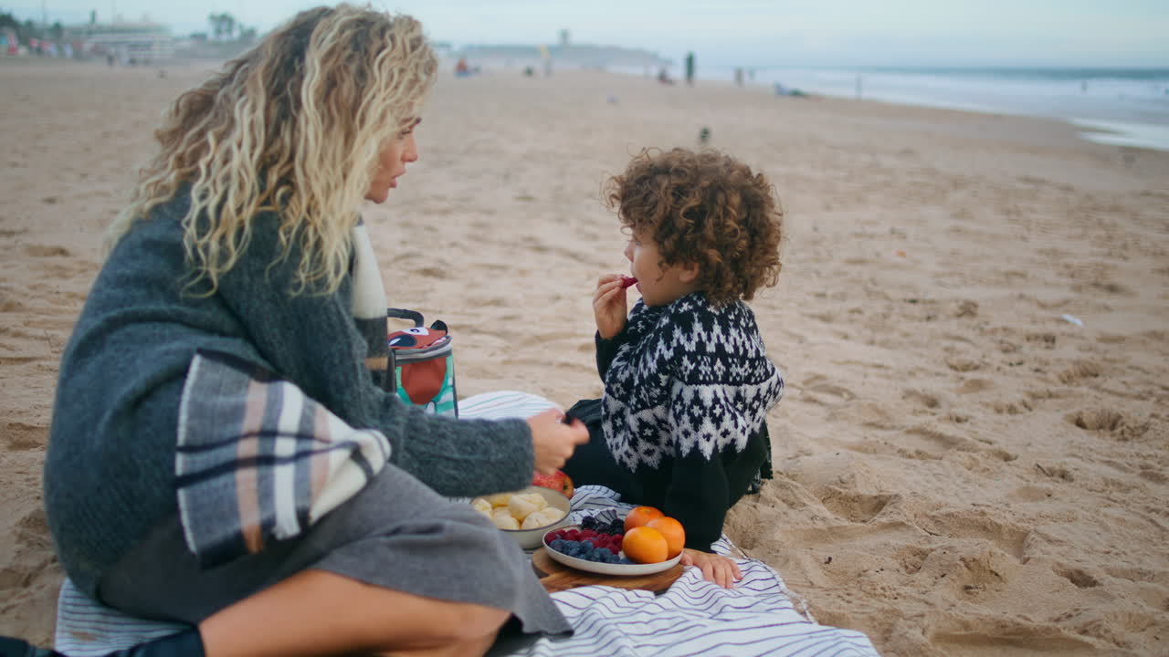 Mor nyder picnic med sin søn på efterårets havbred. Familien tilbringer tid sammen.