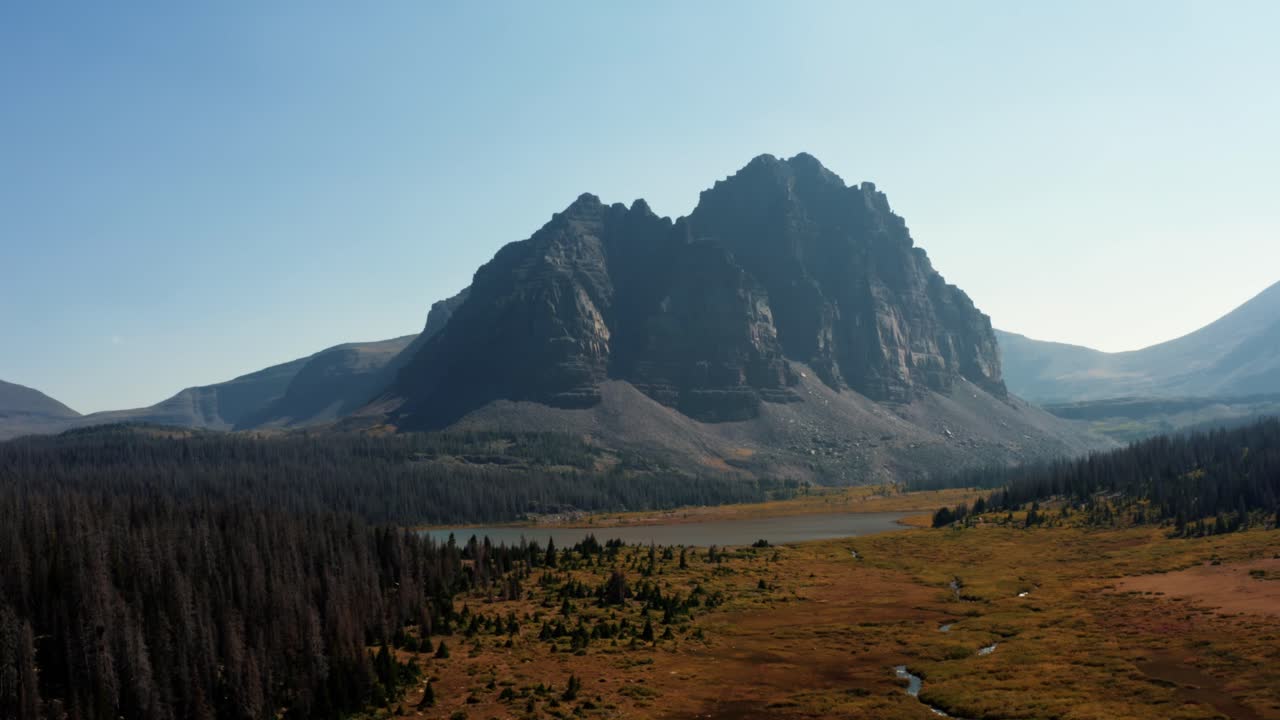Stunning aerial drone landscape nature descending shot of a large meadow with a small stream with the beautiful Lower Red Castle Lake and peak behind up in the High Uinta national forest in Utah