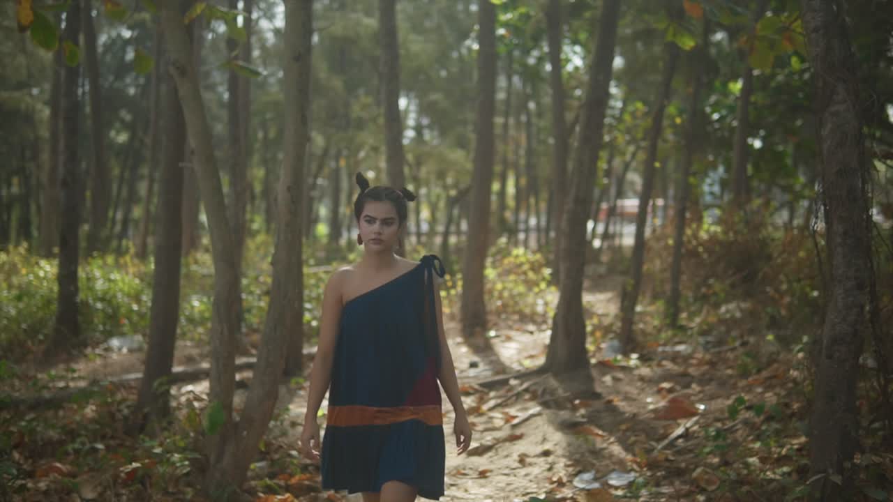 다채로운 드레스를 입은 인디언이 초록색과 조화로운 숲을 걸어가며 배경을 흐릿하게 남 ⁇ 니다.