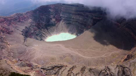 sunny aerial of deep volcano crater lake as cloud begins to roll in