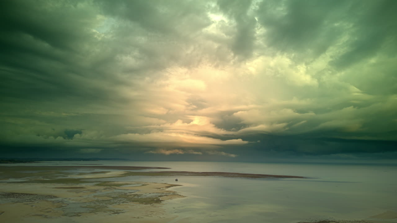 Dramatic aerial view of intense storm clouds and heavy rain over the tropical low tide flats of Bintan Island, Indonesia, with a bright rainbow breaking through the dark storm