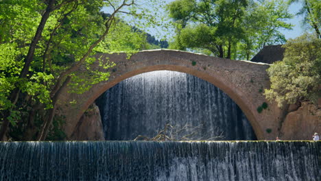 stone arch bridge palaiokarya greece waterfall slow motion windy day