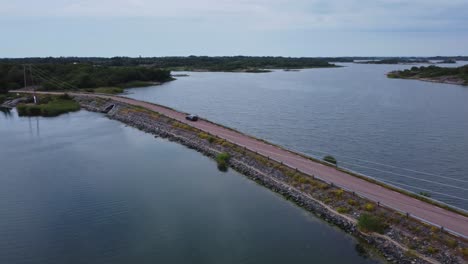 Car-driving-on-a-narrow-bridge-in-Brando-Island-in-Aland-Islands,-Finland,-aerial-spotlight-shot