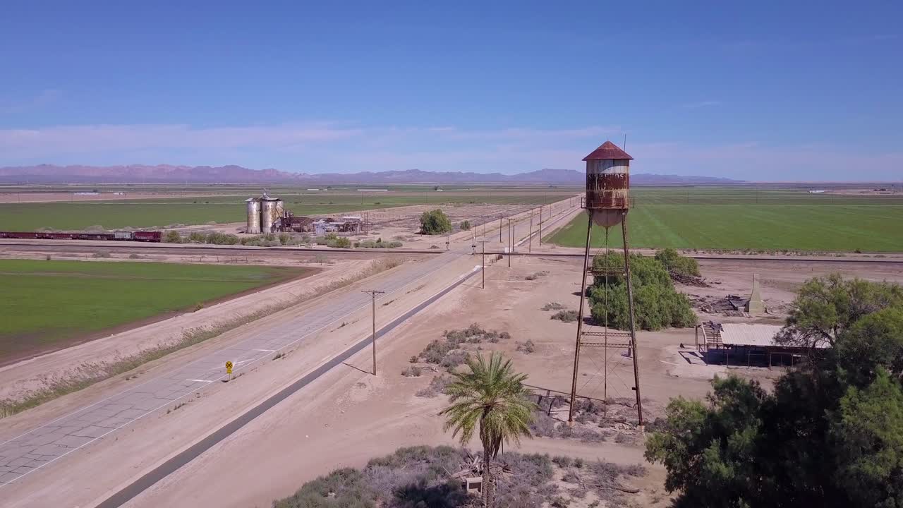 una antena de ángulo alto sobre una carretera solitaria abandonada a través de una zona rural que pasa por el primer plano de la torre de agua