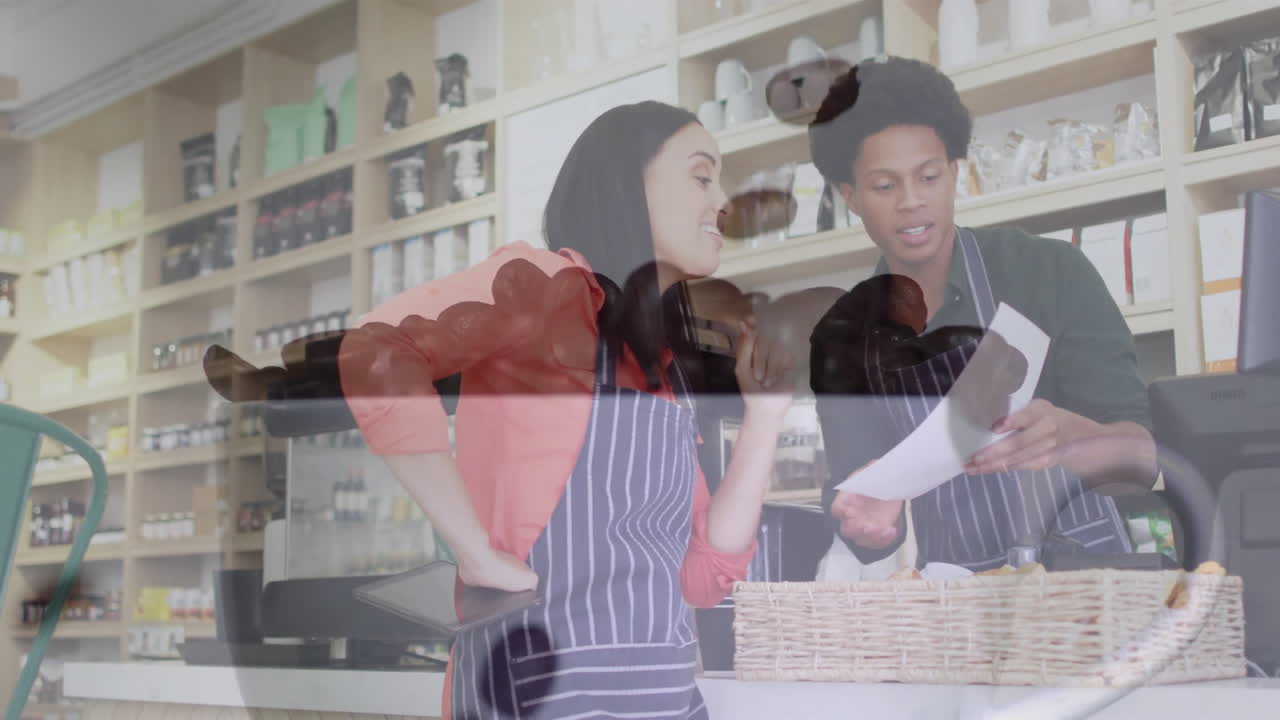 Two co-workers checking order on tablet behind cafe counter, showing floating sales chart