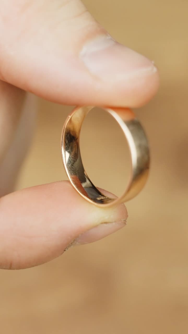 Close-up of fingers holding a gold ring with a warm, soft background