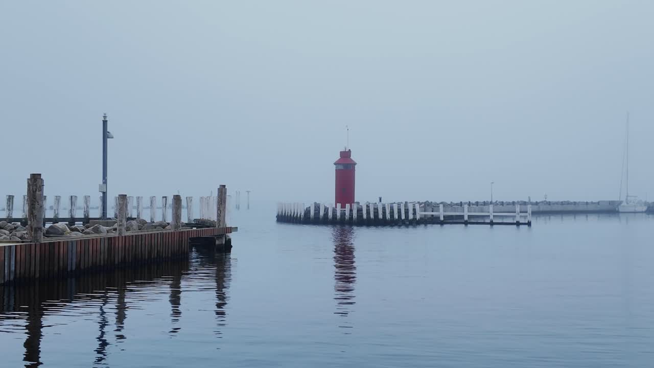 The red lighthouse stands at the entrance of the pleasure boat harbor, partially hidden by the fog. Denmark Scandinavia