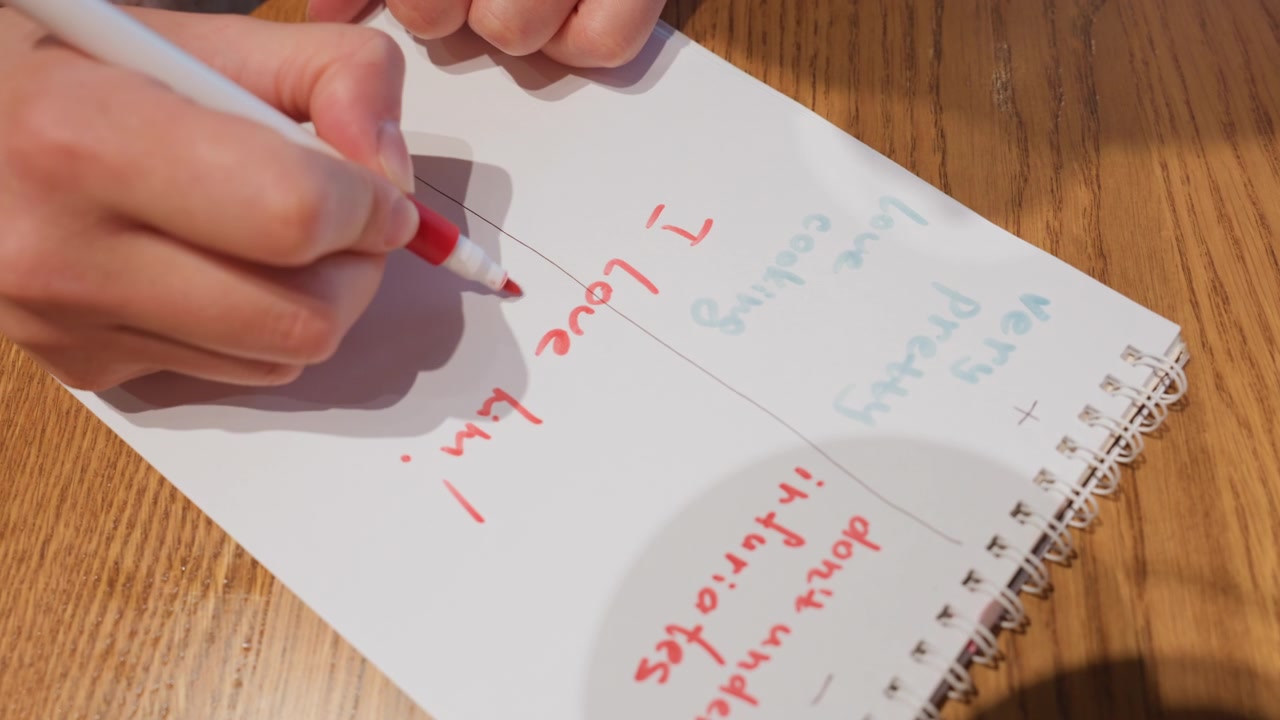 Close-up of Hand Writing 'I Love Him!' with a Red Marker in a Notebook