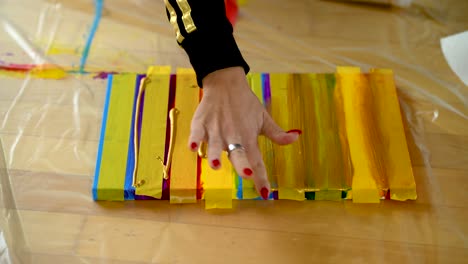 una mujer que usa cinta de pintores para terminar sus rayas de colores en un lienzo