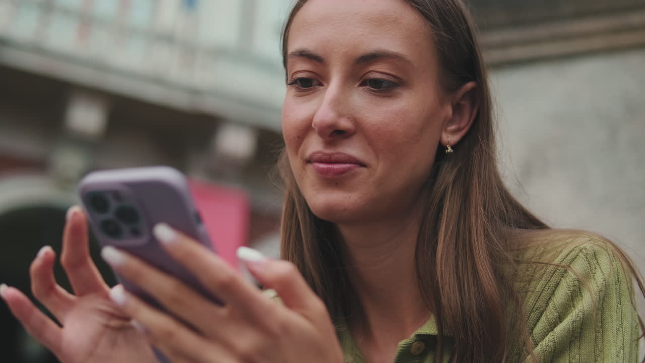Ung kvinde smiler, mens hun bruger sin smartphone udendørs