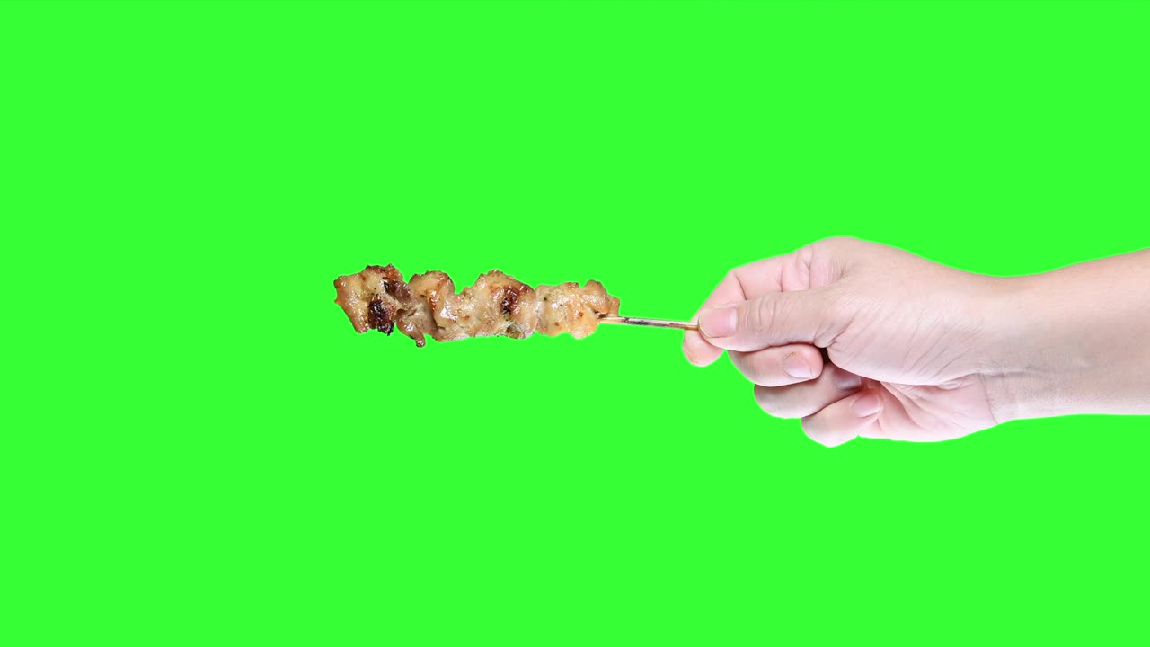 초록색 스크린 배경에 바베큐 사타이 을 들고 있는 손.