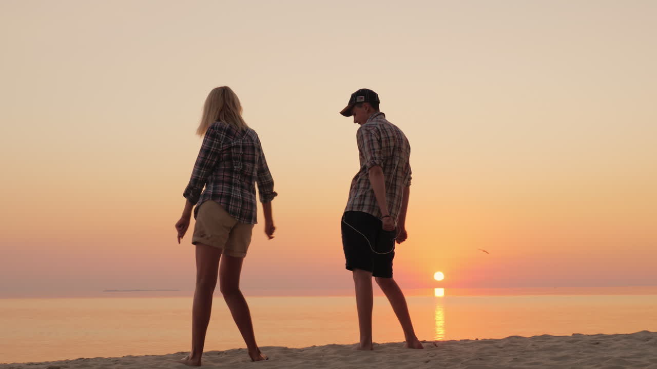 한 여자와 그녀의 십대 아들이 함께 해변에서 재미있는 춤을 추며 세련된 춤 동작을 배웁니다.