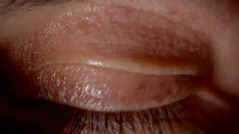 un primer plano de una persona caucásica con ojos marrones parpadeando y mirando con calma a la cámara en la oscuridad.