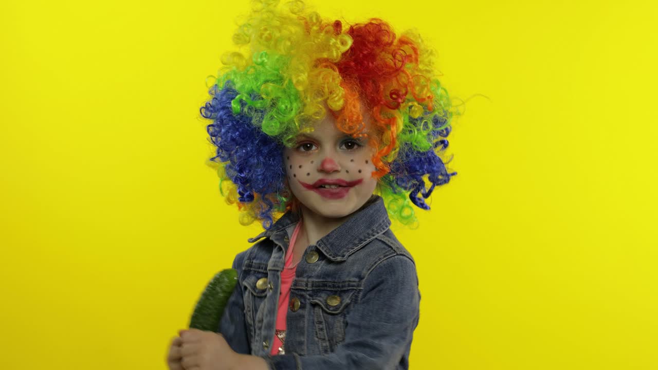 una pequeña niña payasa con una peluca colorida haciendo caras tontas, cantando, sonriendo, bailando. halloween