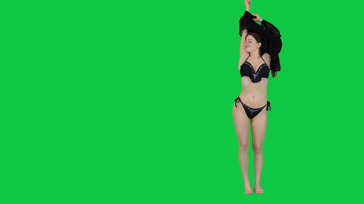 Beautiful female model takes off her dress to reveal bikini in front of a green screen