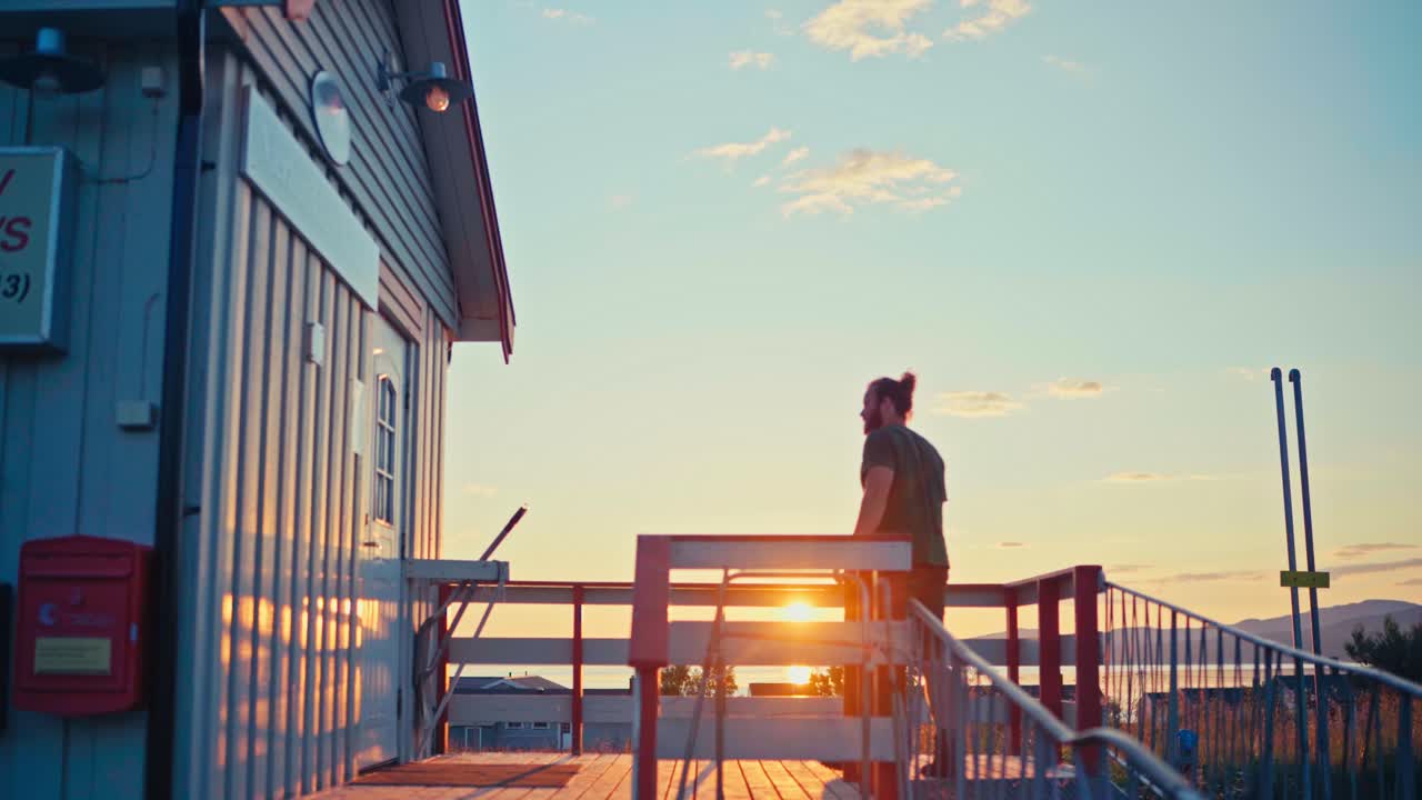A Man Walks to a Nearby Shop as the Sun Sets in Kokelv, Hammerfest, Finnmark, Norway - Static Shot