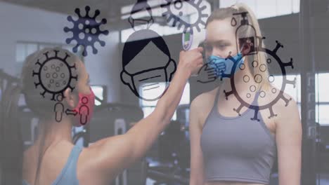 iconos del concepto de coronavirus flotando contra una mujer midiendo la temperatura de una mujer caucásica en el gimnasio