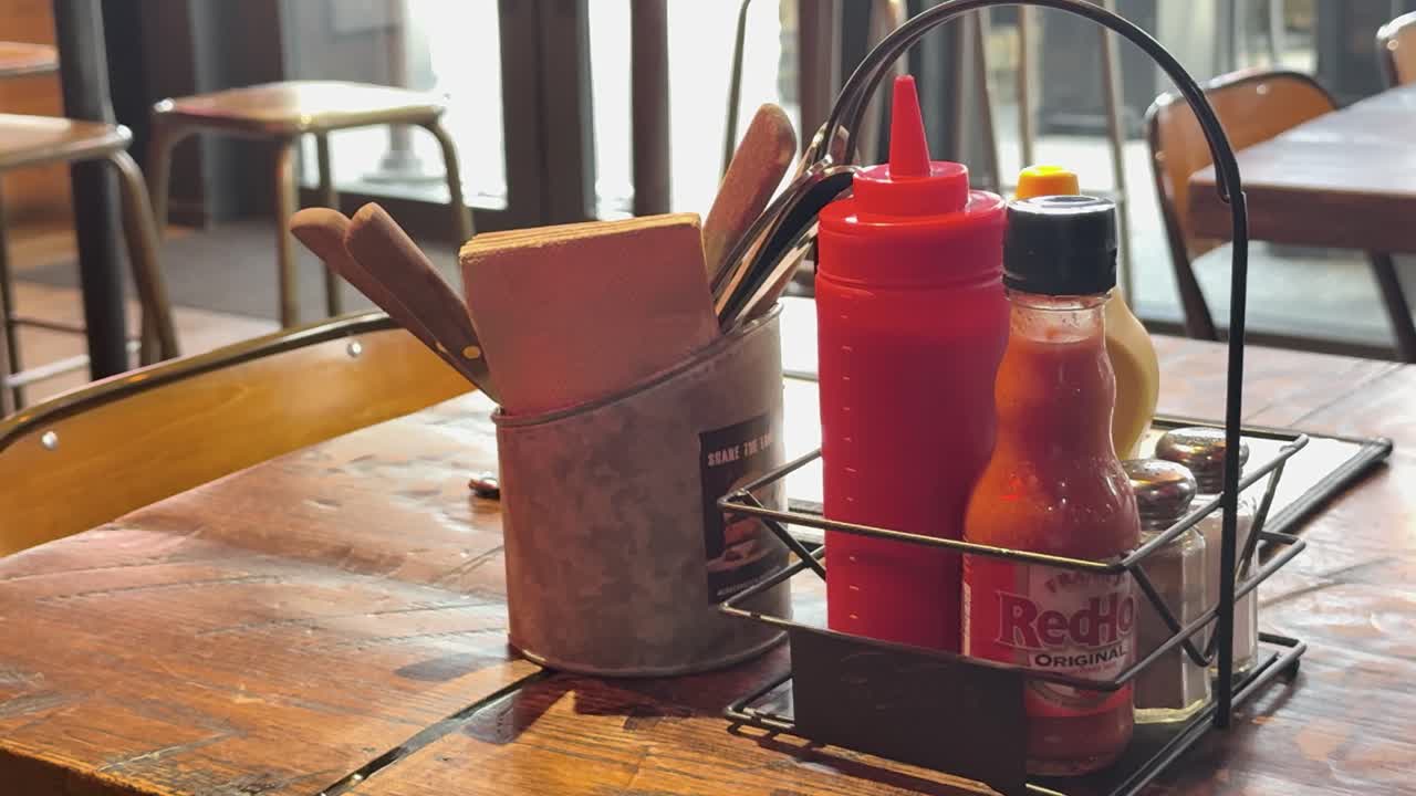 A hand rearranges condiments on a wooden table in a sunlit cafe, creating a cozy dining atmosphere