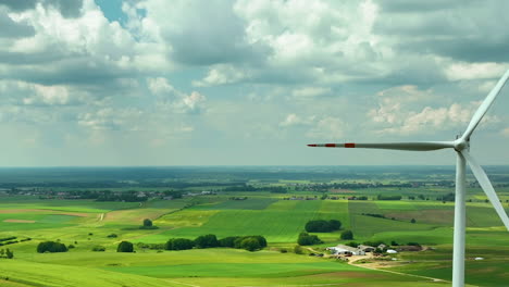 Aerial-footage-capturing-a-single-wind-turbine-in-the-foreground-with-a-vast,-green-rural-landscape-and-partly-cloudy-sky-in-the-background,-emphasizing-renewable-energy-integration