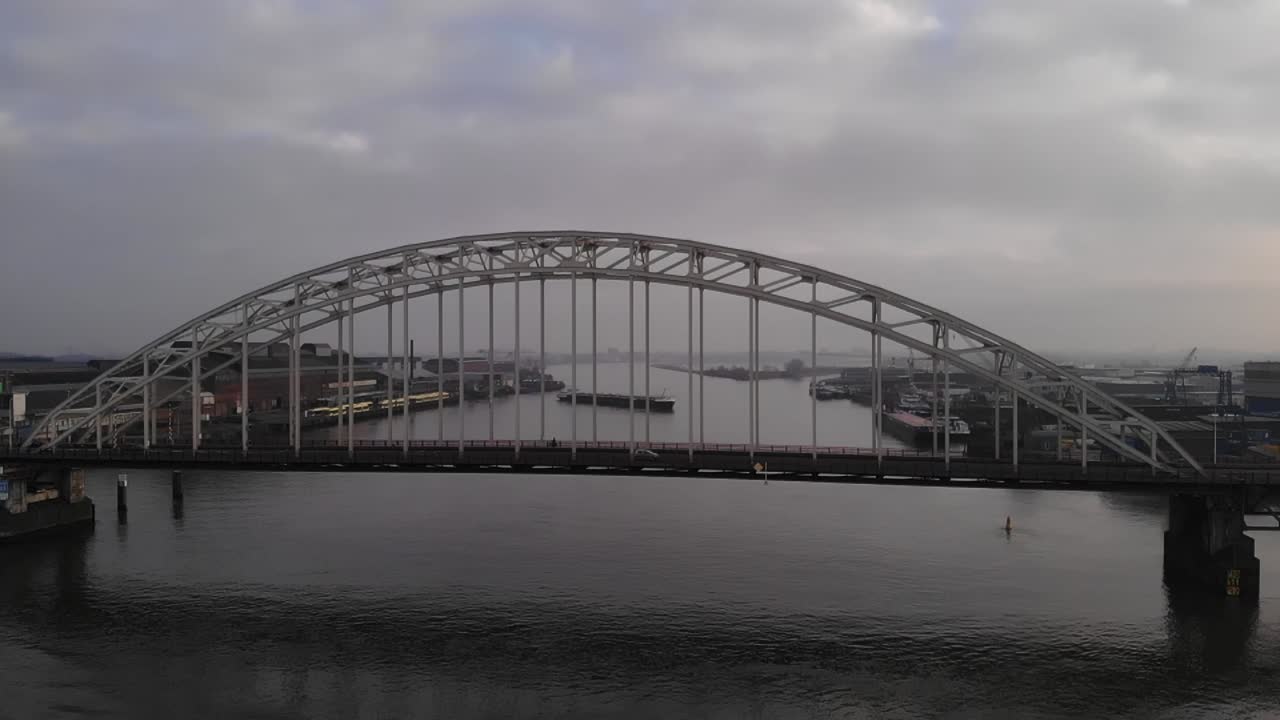 Cars and a truck driving on a bascule bridge with on the background a barge which is turning on the Dutch river Noord on a cloudy day. Pedestal drone shot