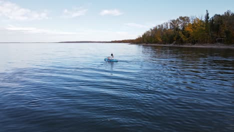 woman kayaking on a large blue lake in front of autumn foliage in alberta, canada