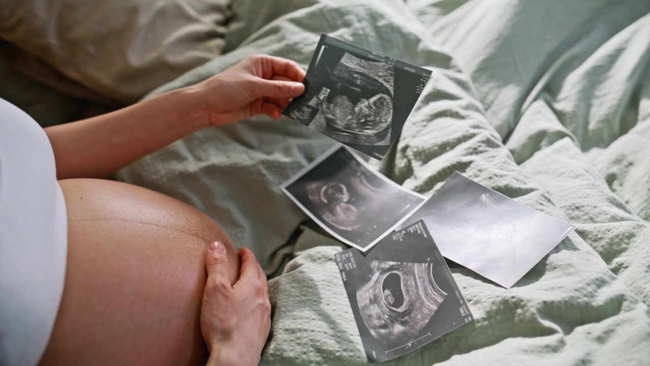 Madre in attesa che esamina ecografie sul letto. Primo piano di una mano che tocca la pancia.