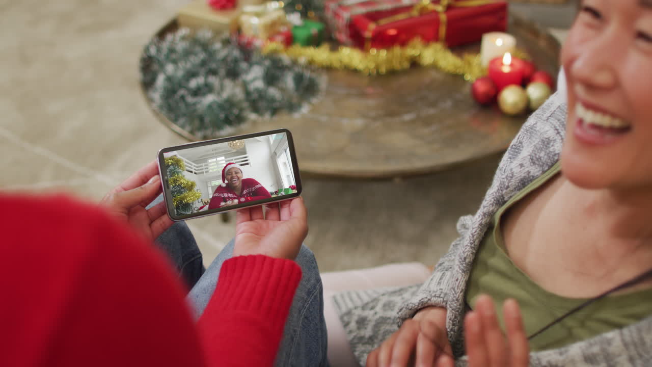 스크린 에 있는 여자 와 함께 크리스마스 비디오 통화 를 하기 위해 스마트폰 을 사용하는 웃는 아시아 커플