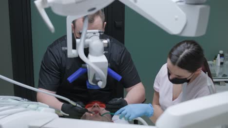 male dentist working with dental microscope in modern stomatology clinic. doctor using microscope for root canal treatment. stomatologist performs a surgical operation. cosmetic dentistry and surgery.