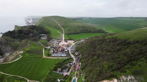 Vuelo-Sobre-El-Pueblo-De-Lulworth-En-La-Costa-Jurásica-De-Dorset-Con-Vistas-A-Los-Acantilados-Distantes-Y-Al-Paisaje-Verde-Y-Ondulado.