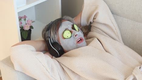 woman with facial mask and cucumbers on face listening to music