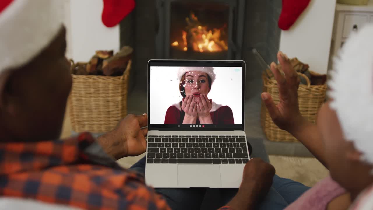 Coppia afroamericana con cappelli di Babbo Natale che usa un laptop per una videochiamata di Natale con una donna sullo schermo