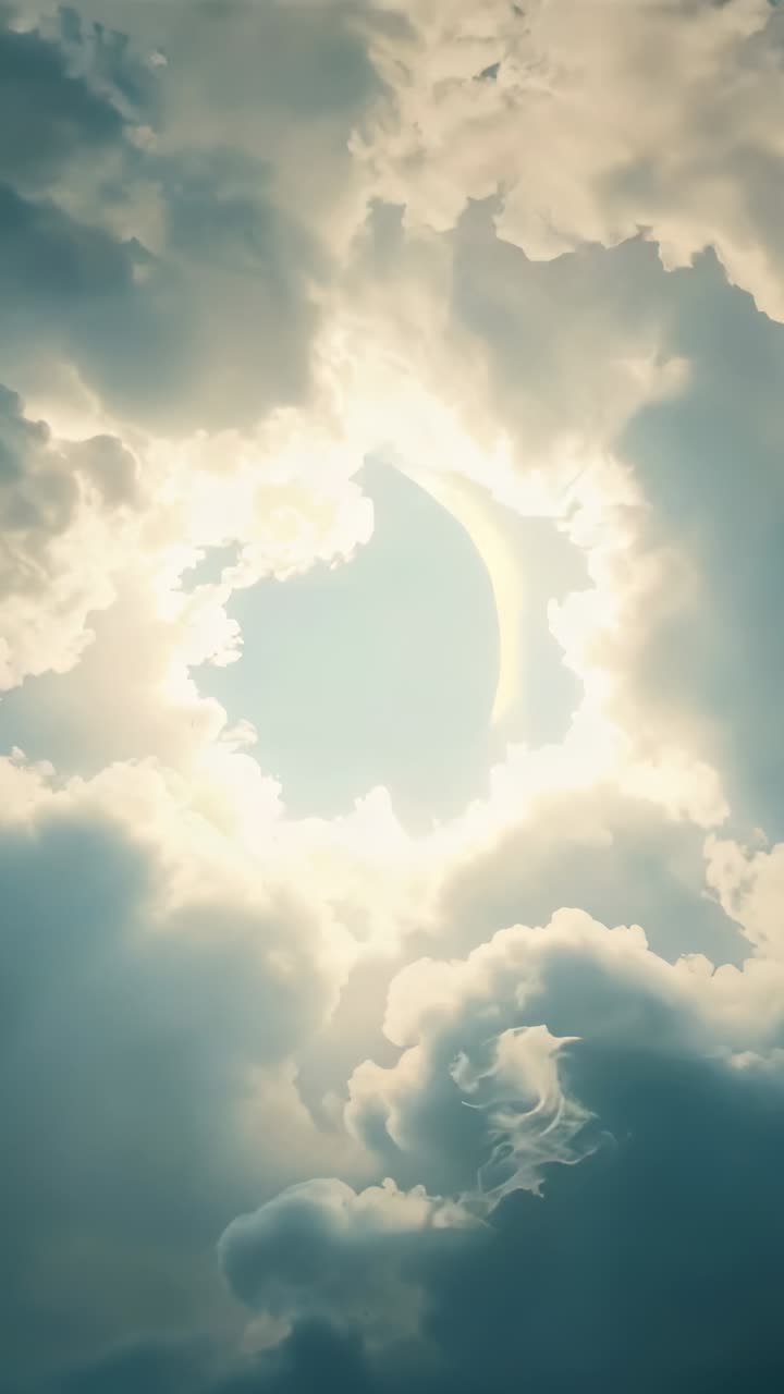 Vertical video: Shifting cumulus clouds exposing bright disc in blue sky, revealing glowing halo