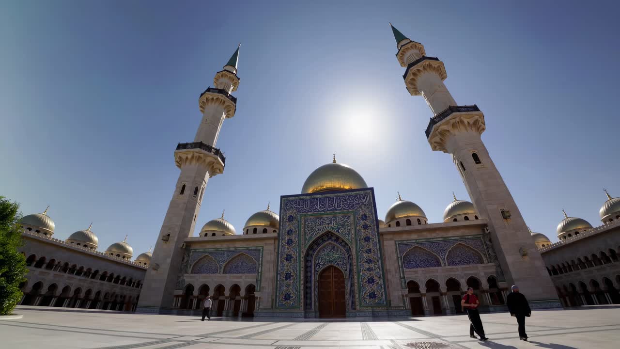 Video girato dal basso che mostra una grande moschea con facciata a mosaico elaborata e minareti imponenti