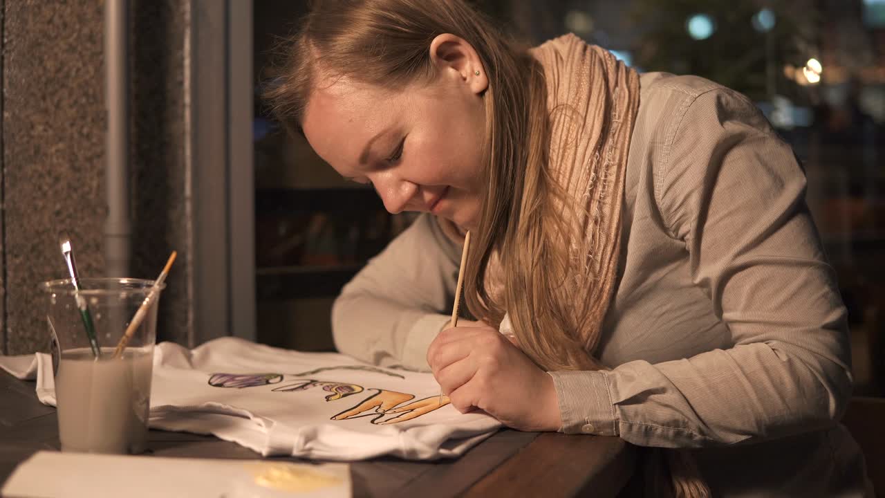 Mulher pintando um desenho em uma camiseta em um café à noite