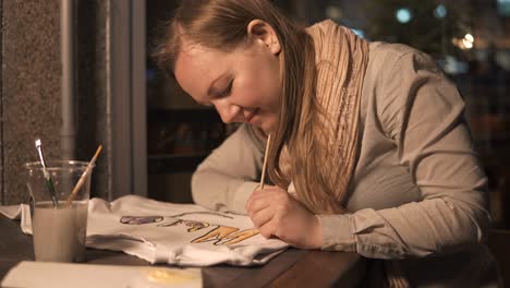 woman painting a design on a t-shirt in a cafe at night