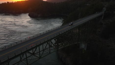 Aerial-shot-of-an-SUV-driving-across-Deception-Pass-at-sunset-on-a-warm-summer-evening