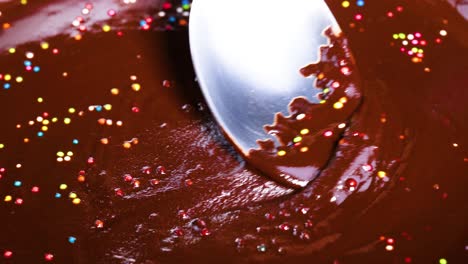 spoon stirring chocolate with colorful sprinkles