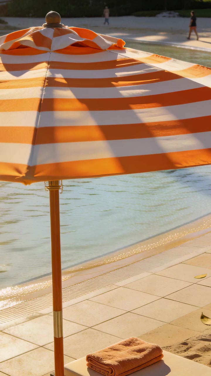 Video verticale: Inquadratura di ombrellone e asciugamano a bordo piscina, luce solare che si sposta, adulti che camminano per svago.