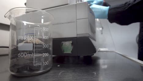 el trabajador de laboratorio prepara una muestra de sedimento de mineral para su análisis con un vaso de precipitados