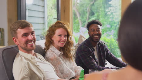 multi-cultural group of friends sitting on sofas at home together enjoying drinks and talking