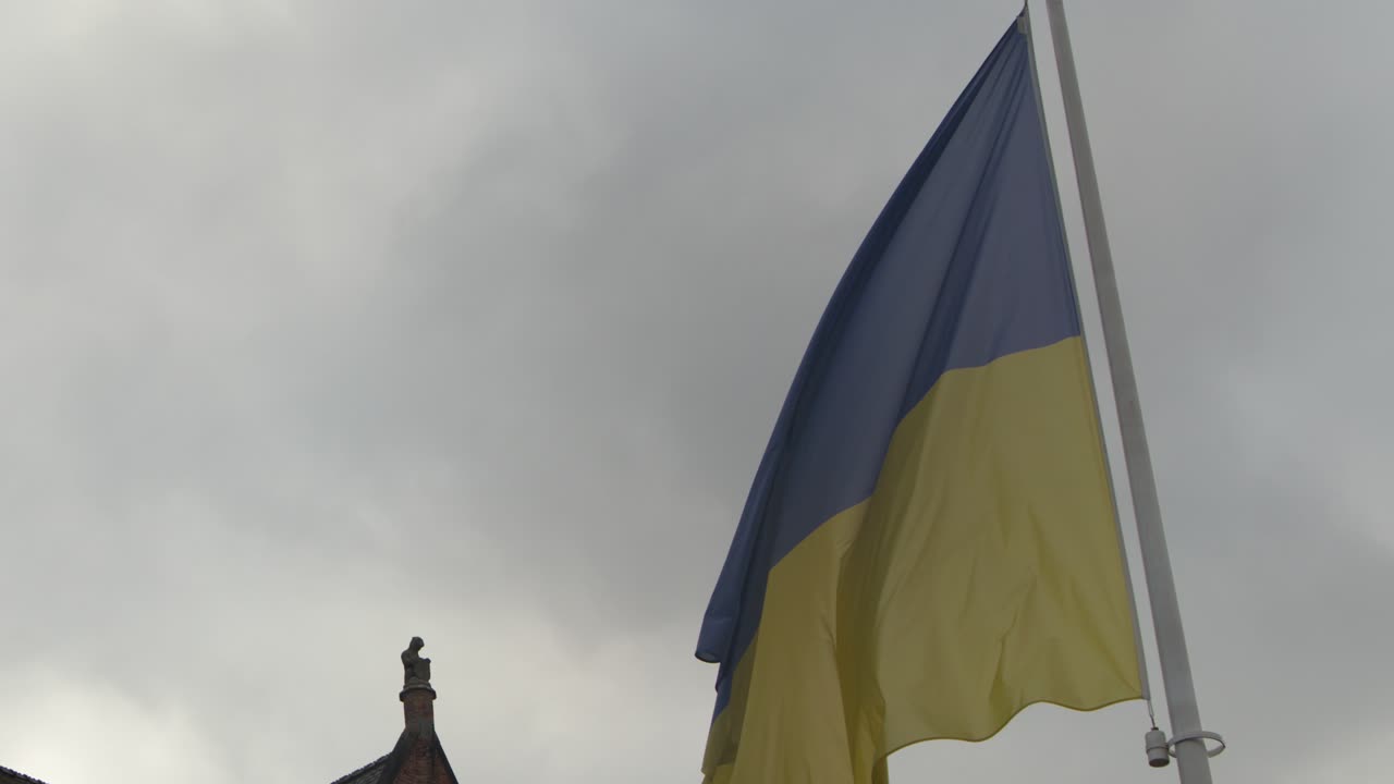 Ukrainian flag flutters against medieval Bruges architecture, overcast sky, steady camera, natural lighting