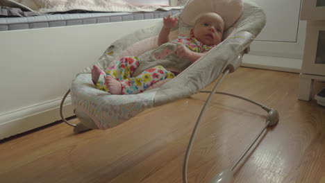 awake and active baby girl in bouncy seat at home