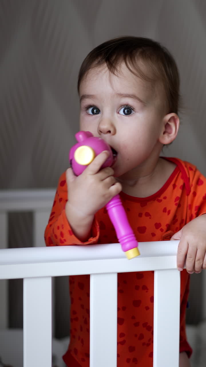 Female hand gives a toy to a baby standing in the crib. Sweet little baby takes a toy and shoves it to his mouth looking up. Close up. Vertical video