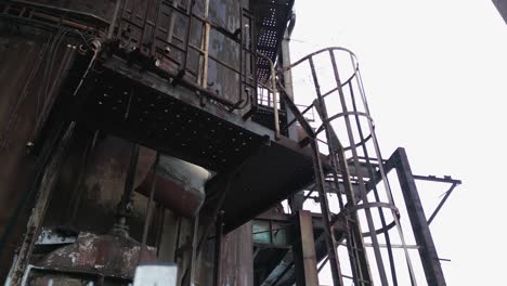 abandoned and rusted industrial structure with a spiral staircase attached to its side