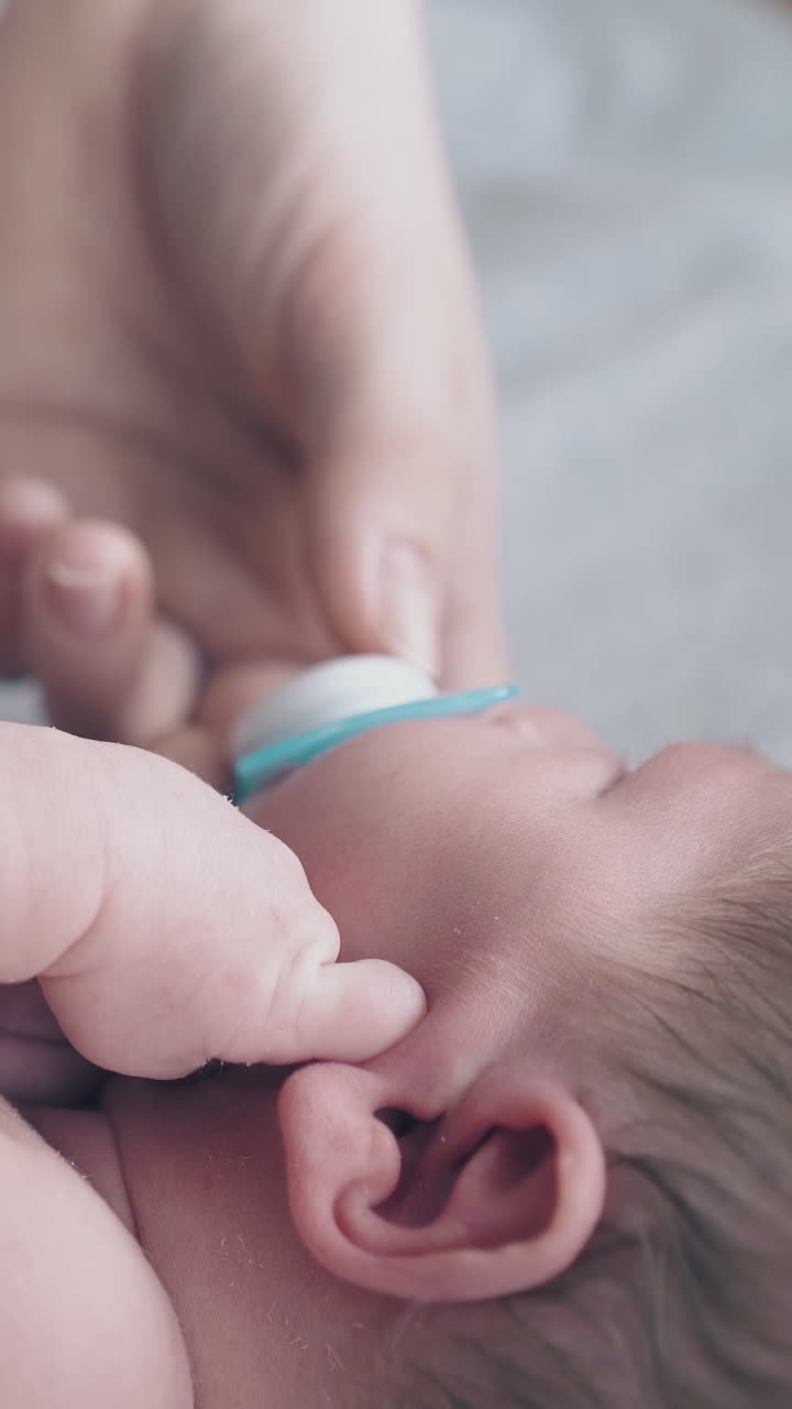 mother hand calms down restless infant with short blonde hair and in white diaper holding small pacifier close view