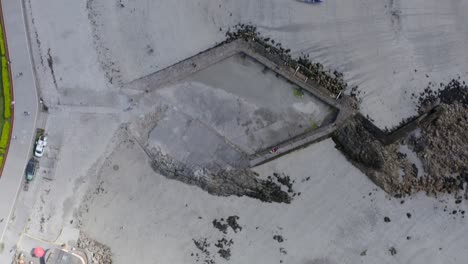 Top-down-aerial-bird's-eye-view-above-tidepools-at-ladies-beach-galway,-and-currach-boats