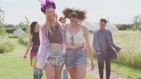 group of excited young female friends walking through music festival site