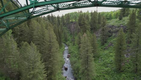 drone flies under a green painted steel bridge