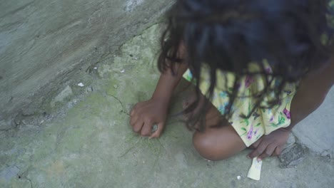 young indian poor orphan girl playing with stone on ground, rural village