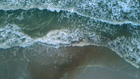 Aerial-shot-of-beautiful-blue-green-ocean-waves-crashing-on-sandy-beach-zoom-out
